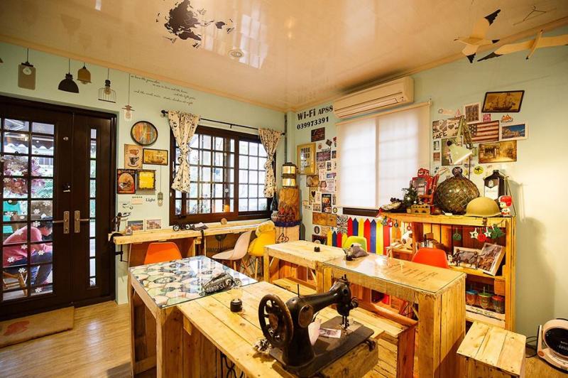 在這個咖啡館中堆滿著許多小雜物，桌上放著一台古老的裁縫機，桌邊的架子放著照片、帽子等物品。