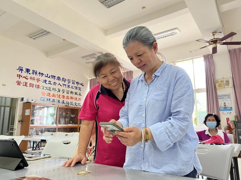 學員專注地使用智慧型手機拍攝老照片，旁邊桌上還擺放著幾張泛黃的舊照片，充滿時光的痕跡。