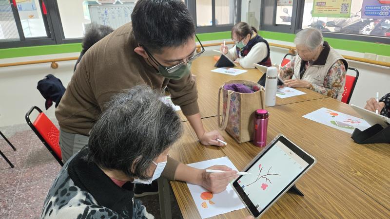 棋盤社區關懷據點的教室裡，阿嬤坐在桌前，手裡握著觸控筆，小心翼翼地在平板上描繪著色彩繽紛的圖案。她們一邊對照著範本圖案，一邊在平板電腦繪圖APP上慢慢勾勒線條，臉上透著認真的神情。老師溫柔地在旁指導，有時彎下身子輕聲說明，有時鼓勵阿嬤幾句。