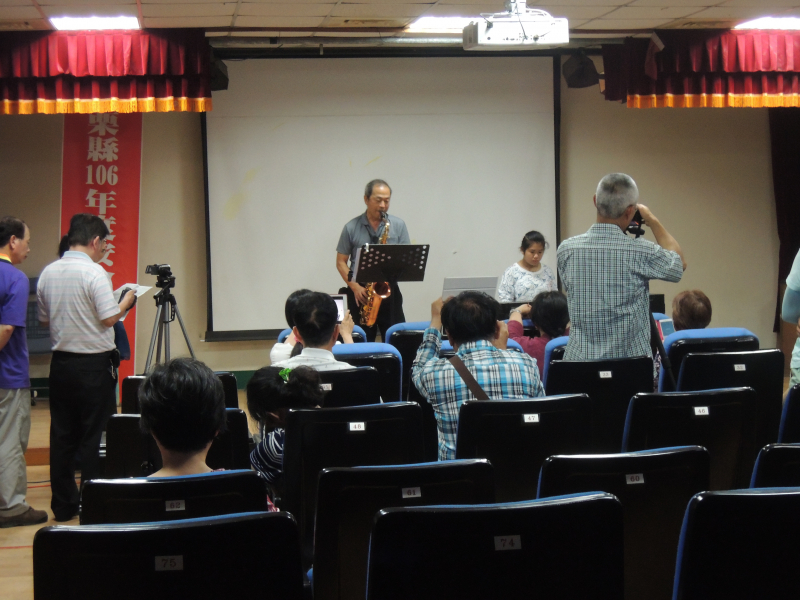 長青老師在台前薩克斯風吹奏，台下學員們拍攝