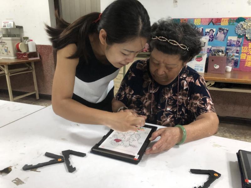 教學阿嬤使用平板用觸碰筆來點擊色塊。