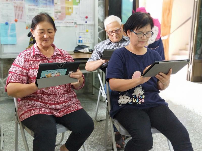 兩位阿嬤和一位爺爺面帶著笑容，目不轉睛盯著手上的平板。