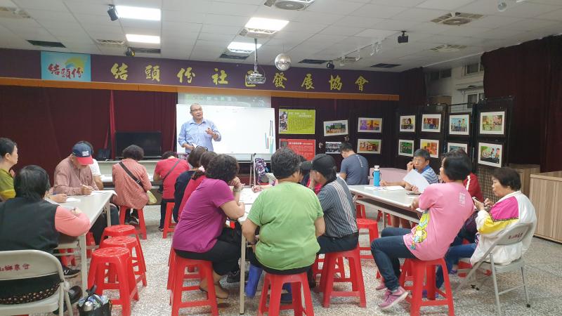 結頭份社區活動中心裡，講師在投影幕前教授直播技巧，前方有三張長桌圍繞著認真的學員。