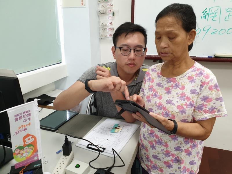 講師站在學員的右邊，以食指觸碰螢幕，引導學員使用智慧型手機上網。