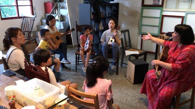 學員與講師在教室內圍坐成一個小圓圈，像是營火晚會一般，年長的學員拿著吉他，年幼的學員則握著烏克麗麗。