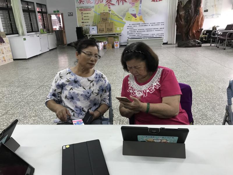 在課程的休息時間，兩位學員彼此討論授課內容，右方身穿紅衣的學員拿出手機開啟程式詢問。