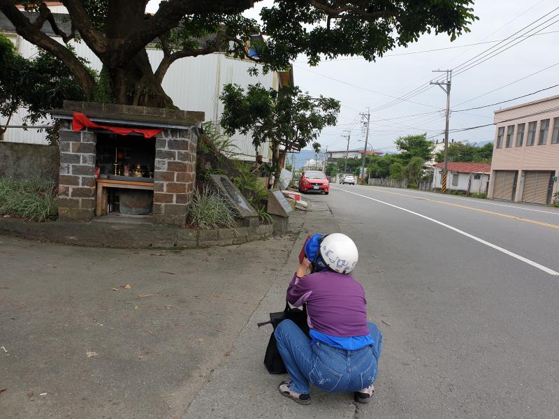 學員剛下機車直接蹲在地上拿出相機拍攝小廟的環景照片。