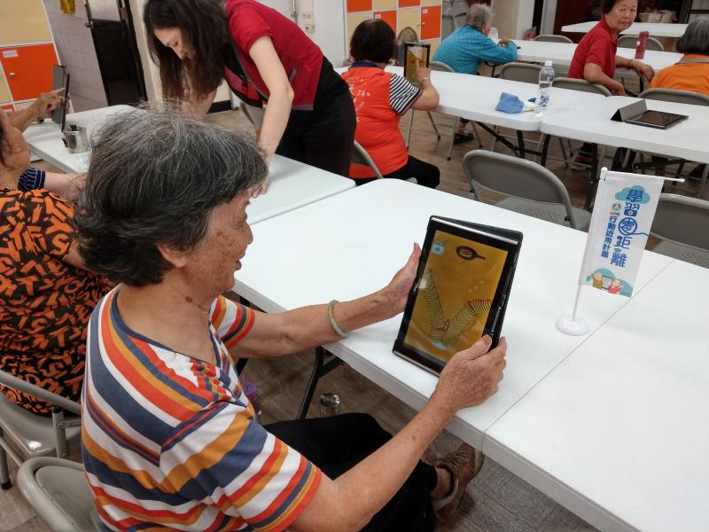 一位長輩學員正在以近用計畫提供的平板，玩著應用程式鬆餅塔，藉此熟悉平板電腦的使用方式。