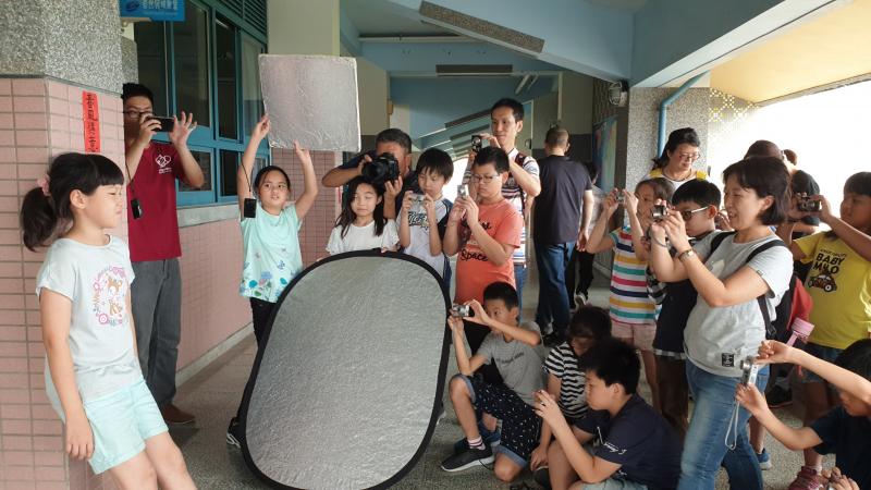 講師攤開大大的反光板，將光源反照在模特兒身上，並讓其他學員圍觀攝影。