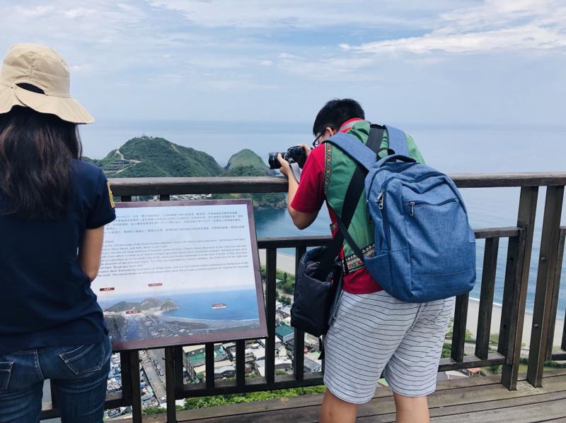 老師帶學生至高台上，向下拍攝高處風景，學員拿著自己的單眼相機向遠方拍攝。