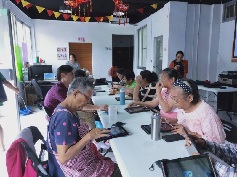 年長的學員們將平板平放於桌上，以雙手摸索並觀察螢幕內的變化。