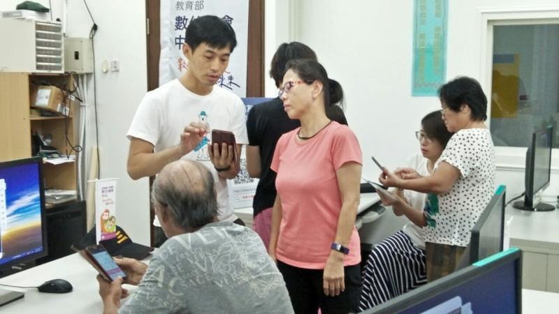 講師正在講解LINE的設定問題給身穿粉色衣服的學員聽。