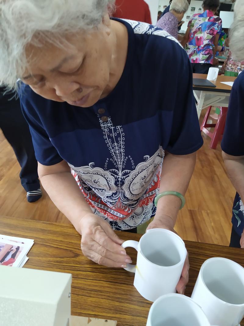 年長的DOC學員看準馬克杯的形狀，準備將它放到熱轉印設備中，將圖片印上去。