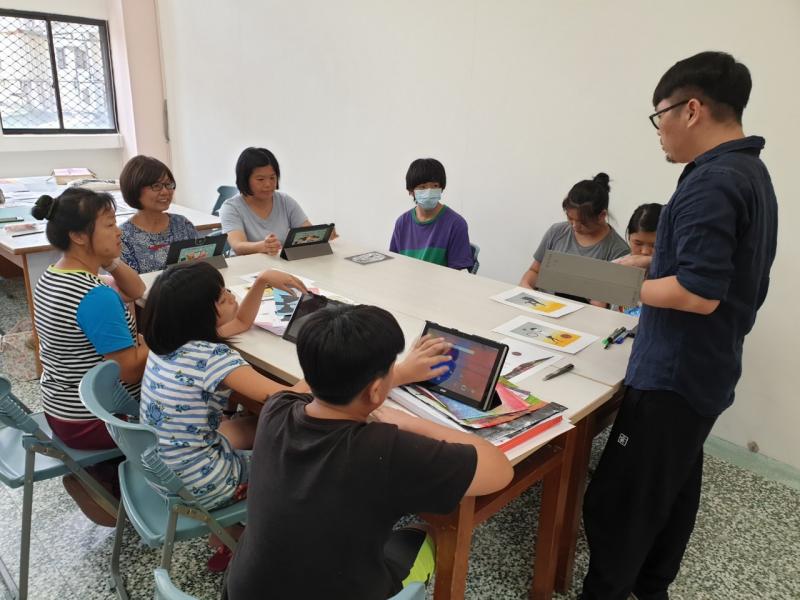 學員圍坐在大方桌前，桌上擺設有平板，講師在眾人前方指示，以平板選取熱轉印用的圖片。