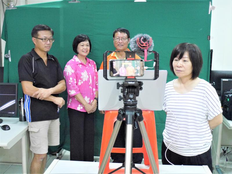 學員和老師在綠幕前，對著手機攝影準備開始錄製主播稿