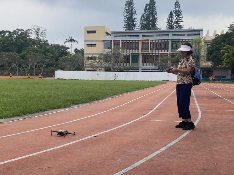 操場上,一位女學員手持手機遙控空拍機