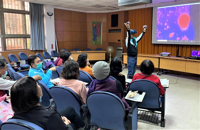 學員手持 VR 設備在前台觀看海底世界，台下學員看著台上同步投影的內容