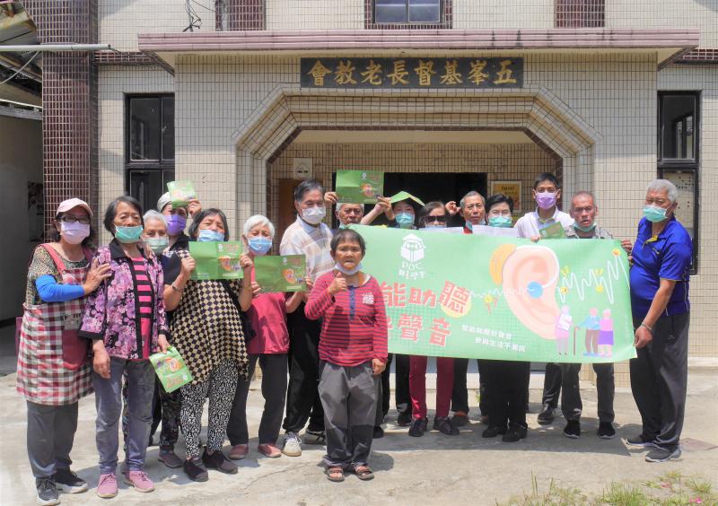 一群人舉著智能助聽好聲音的綠色大海報一起拍照，手比出聽的姿勢