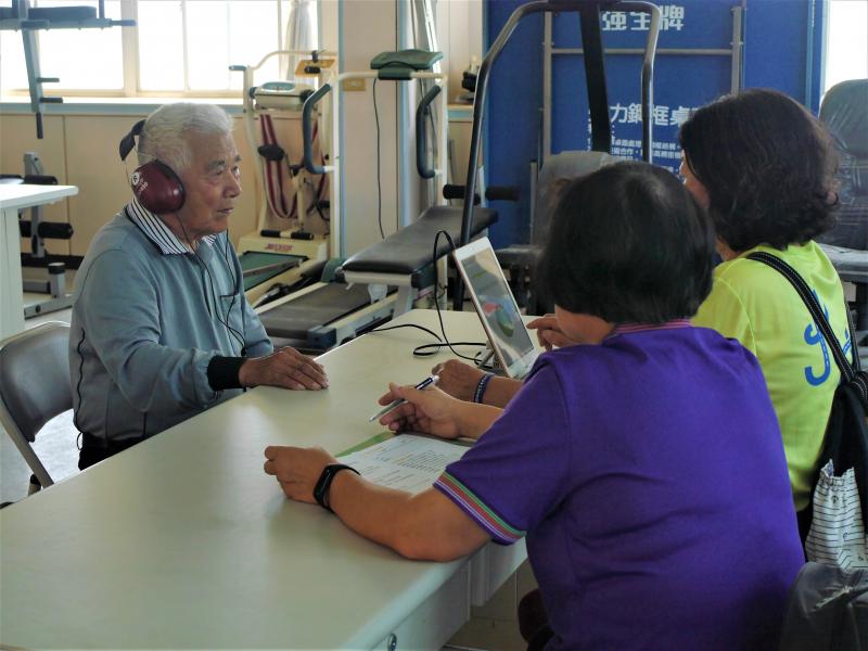 兩位女學員在桌前為一位男性長輩進行聽力篩檢