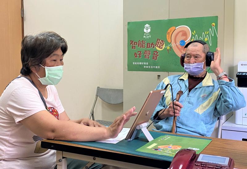 一位女性志工協助一位男性長者進行平板聽力篩檢