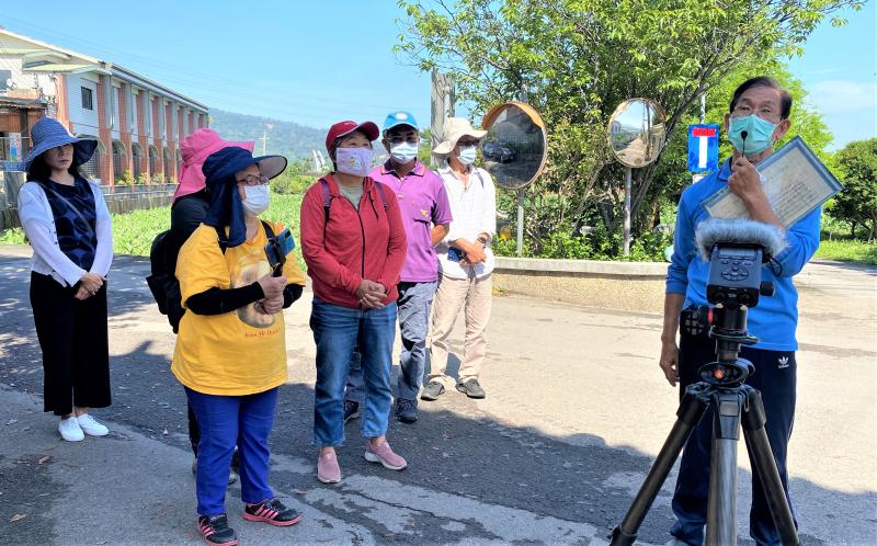 一群人聽著總幹事講解社區，一旁的學員並同時進行素材收集拍攝