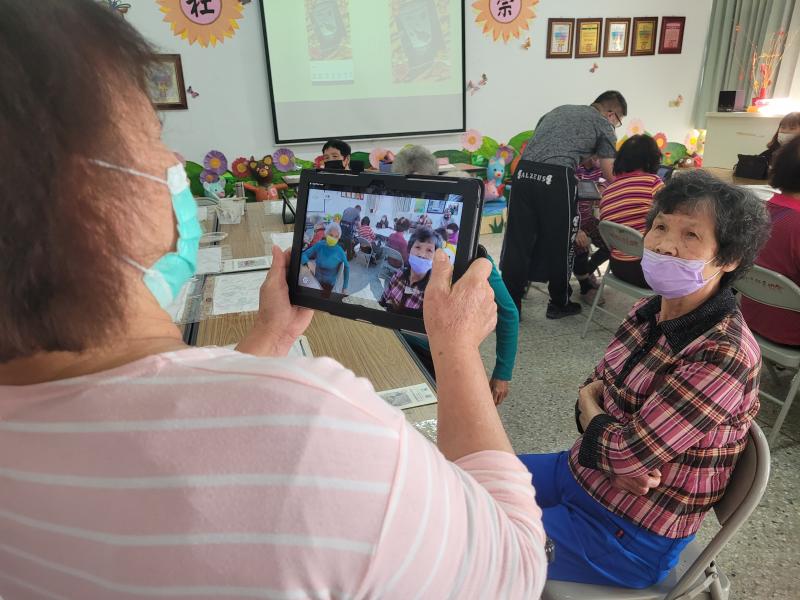 學員試著站著拿起平板拍攝著旁邊學員