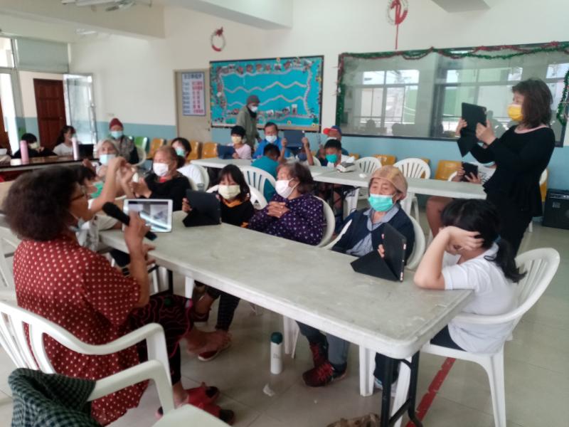 學員阿嬤帶領大家唱歌，另位學員則拿著平板進行全部學員歌唱的錄影