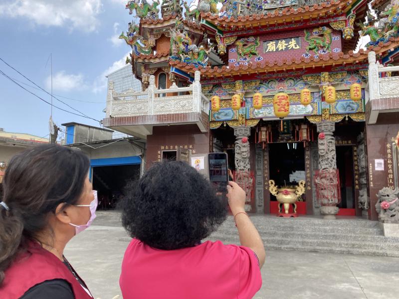 長輩拿著手機，來到廟宇前面，開始介紹歷史