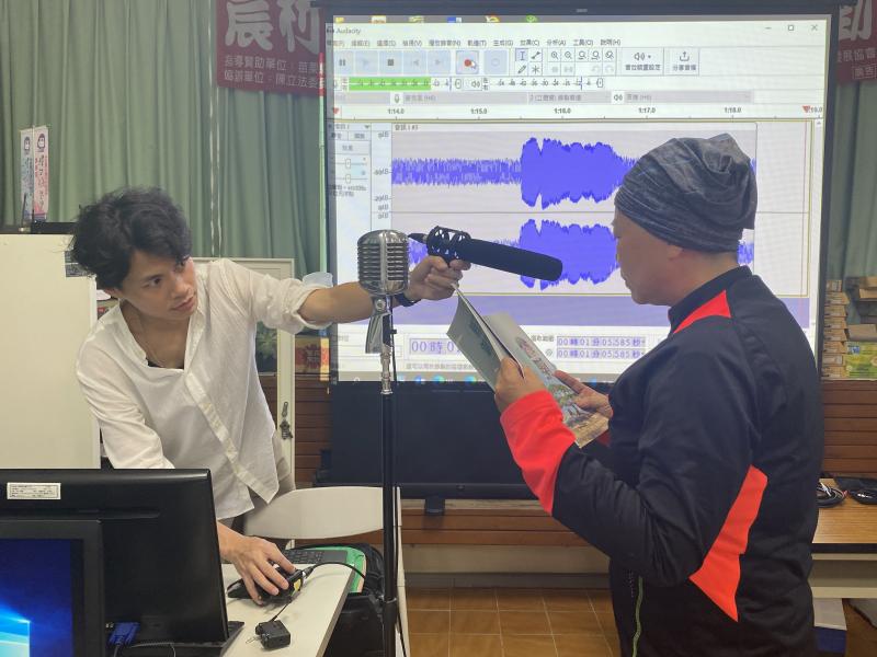 在麥克風前練習讀稿的學員與旁邊協助的老師