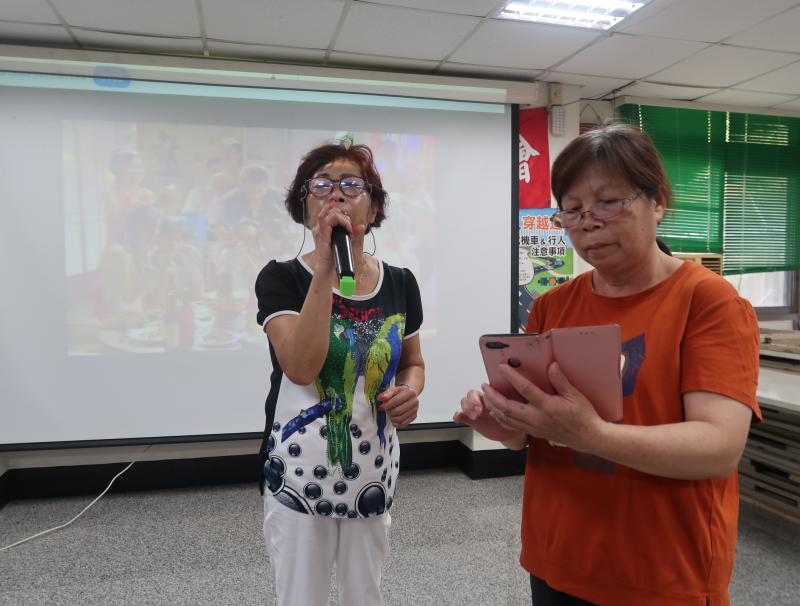 湯綠芽老師用手機點歌給楊麗月學員唱歌,並示範數位點唱功能。