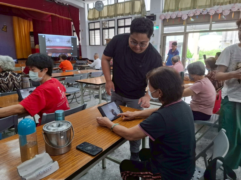 實作環節中，講師走入學員之間進行一對一指導，協助長者操作平板相機進行拍照練習，並解說拍照構圖與拍攝技巧。透過反覆練習與即時回饋，幫助學員建立操作信心，同時提升使用數位設備解決日常問題的能力。