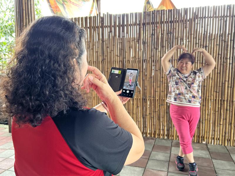 一位學員使用手機為另一位學員拍攝人像照片，學員擺出俏皮可愛的姿勢，作為後續影像合成練習的素材。