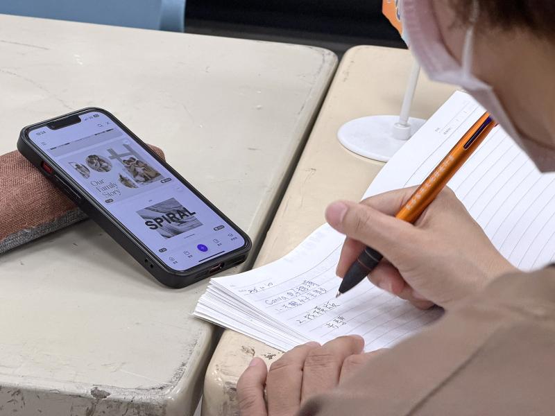 學員依照講師的教學步驟操作手機練習，並將重點步驟整理抄寫在筆記中。