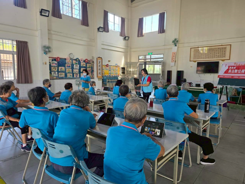復興社區智慧圖片課程中，執行長於台前詳細解說操作步驟，學員專注聆聽，桌上平板顯示數位介面準備實作。