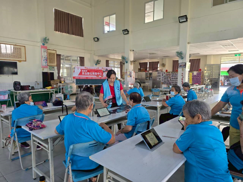 復興社區智慧圖片課程，學員平板顯示花卉線條圖案，執行長巡視並提供個別指導，長輩專注觀看數位螢幕。