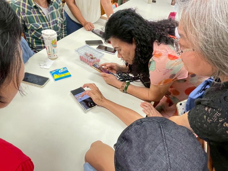 學員圍坐在白色長桌,目光齊聚在手機螢幕上,老師實際操作教導修圖技巧。