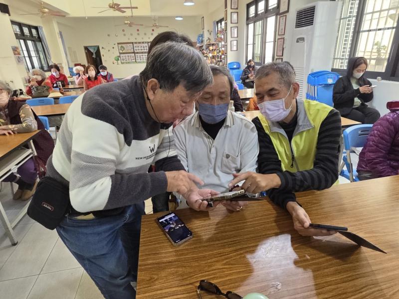 講師與學員近距離討論，指著手機螢幕進行語音搜尋實作教學，互動氣氛認真。