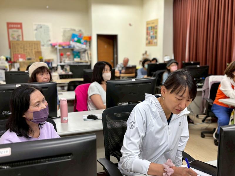 課堂上，學員正專注地在筆記本上記錄剪輯重點，神情認真。後方其他女性學員也正凝視著電腦螢幕或與旁人交流，展現出學員積極參與數位學習的態度。