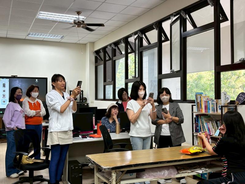 實際練習實況。多位學員聚集在教室一角，講師指導現場拍攝零食開箱影片，其他學員在旁觀摩學習。