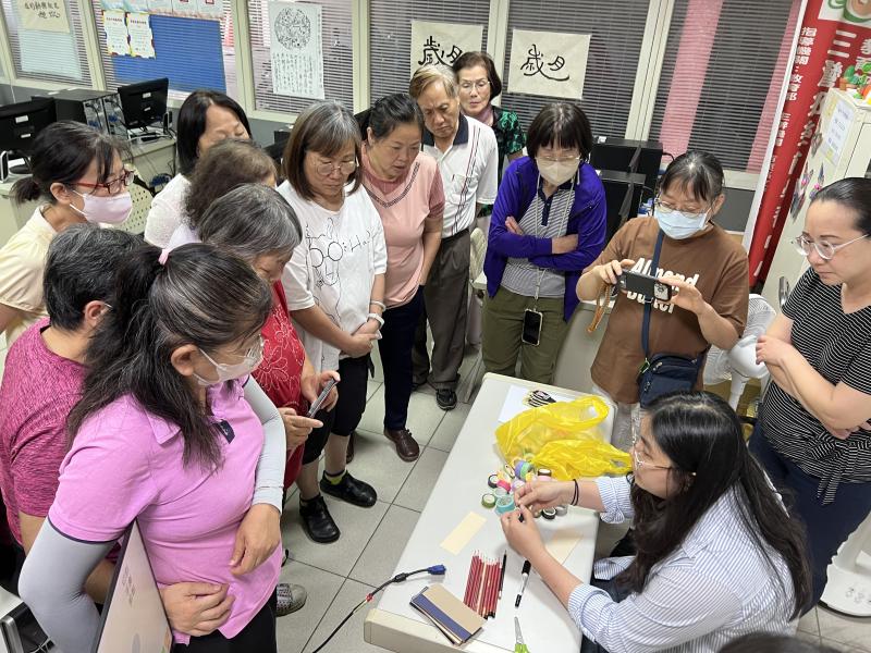數位印花創客課程於三灣農會進行,學員圍聚在桌旁,由講師展示紙膠帶、色鉛筆等印花創作材料,現場氣氛熱絡。