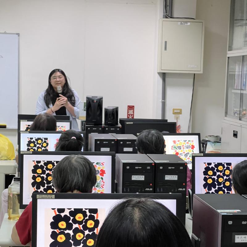 講師邱鉯嵐於電腦教室以投影螢幕展示印花品牌案例,學員在電腦前專注聆聽,學習數位印花品牌分析與圖案發想方法。