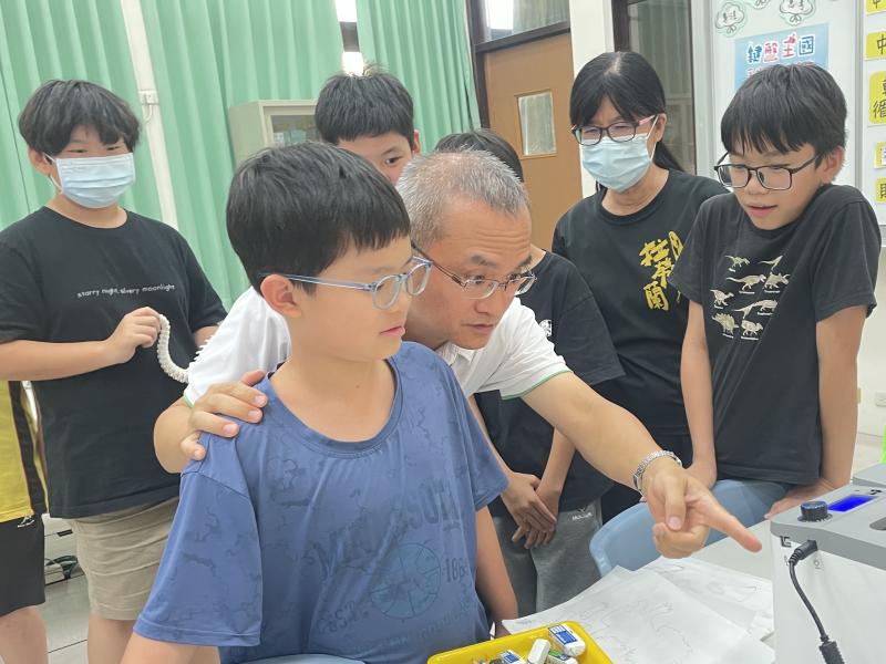 長溫柔地搭著孩子的肩膀,親子一起專注看3D打印機形成的過程。