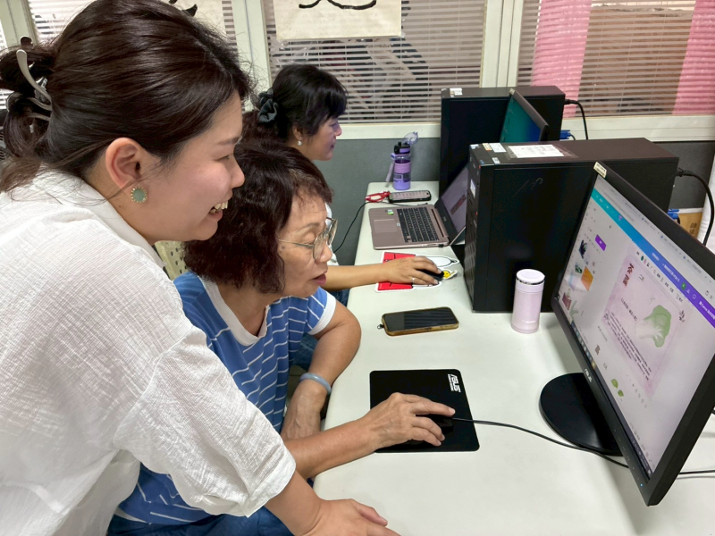 老師俯身緊靠學員，兩人一同凝視電腦螢幕上的 Canva 設計畫面，另一位學員在後方專注操作，神情投入。