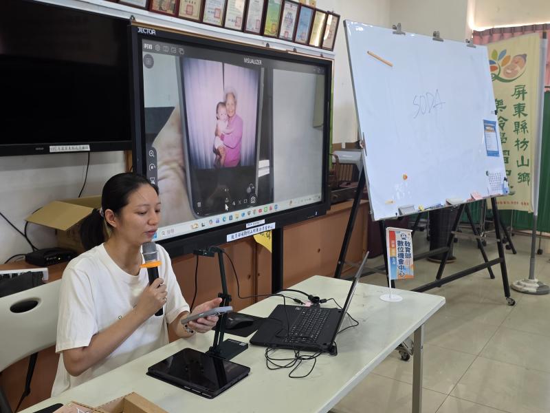 講師於課桌前使用投影設備，在大螢幕展示過世阿嬤與孩子AI合成擁抱的溫馨舊照片並進行講解。